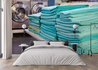 Stack of folded green surgical cloths in an industrial laundry and washing machines behind. Wall mural