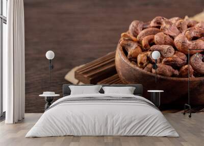 Cashew nuts with peel in a wooden bowl on wooden tray and table background, healthy raw food plate. Wall mural