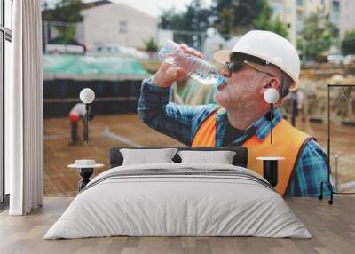 Portrait of a worker, an engineer resting and drinking water after hard work on a construction site Wall mural