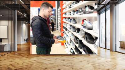 Young man looking for sports equipment at sports shop Wall mural