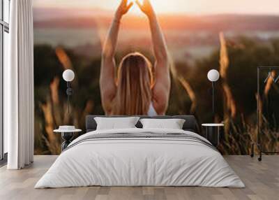 Back View on Woman Sitting in Meditation Yoga Pose and Catching Sun by Hands at Sunset Outdoors Wall mural