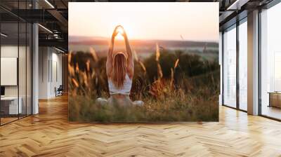 Back View on Woman Sitting in Meditation Yoga Pose and Catching Sun by Hands at Sunset Outdoors Wall mural