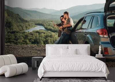 Travelers Couple on a Road Trip, Man and Woman Using Map on Journey Near Their Car Over Beautiful Landscape Wall mural