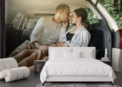 Young Happy Couple Dressed Alike in White T-shirt Sitting in the Car Trunk with Laptop and Popcorn on the Roadside, Weekend Outside the City, Holidays and Road Trip Concept Wall mural