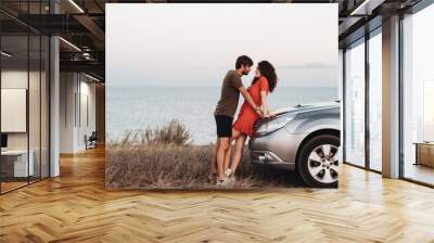 Young Lovers Man and Woman Standing Together Near Their SUV Car on Background of the Sea at Sunset Wall mural