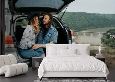 Young Stylish Traveling Hipsters Having Fun Sitting in Car Trunk Near the River Canyon, Travel and Road Trip Concept Wall mural