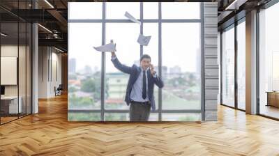 Male business manager throws paper and document to the air to express his emotion after getting good news from the phone call with his partners. Executive officer is frustrated in the office Wall mural