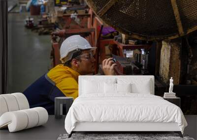 Male mechanical or metallic engineer is using a torch light to check a welding machine for maintenance and quality control. Expert is inspecting or repairing an automatic machine in a metallic factory Wall mural