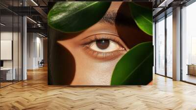 A close-up of an eye partially obscured by green leaves, showcasing a shimmering skin tone in a natural, serene setting. Wall mural