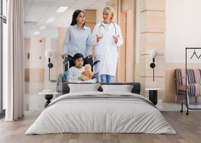 Female pediatrician doctor and child patient on wheelchair with her mother in the health medical center Wall mural