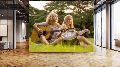 Portrait of caucasian young women sitting in the park outdoor and playing a guitar sing a song together with happiness Wall mural