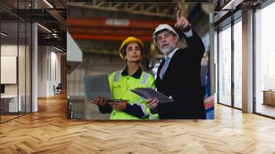 Two people are looking at a laptop, one of them is wearing a yellow jacket. Scene is serious and focused to machine controller board in factory. Wall mural