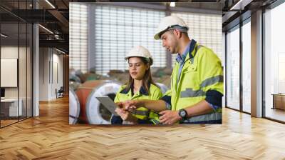 Workers in green uniforms and safety helmets perform quality checks inside a metal sheet factory. Wall mural