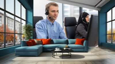 Young man customer service agent with headsets working on computer in a call centre, talking with customer for assisting to resolve the problem with her service mind Wall mural