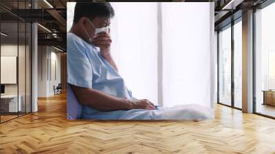 Asian old man is hospitalized with COVID-19. Old male patient wearing a medical mask sits on the patient's bed. Wall mural