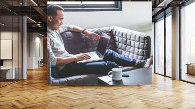 asian young man sitting on sofa and working on laptop at home. Wall mural