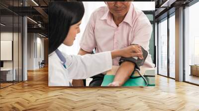 Doctor measuring blood pressure of elderly man in medical office. Wall mural