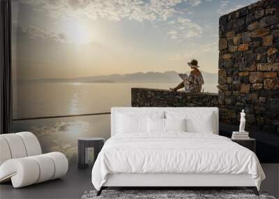 relaxation and meditation concept - woman reading a book near swimming pool with view to the sea at sunrise in luxury hotel Wall mural