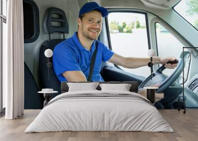 transportation services - young male driver in blue uniform driving a van. smiling at camera Wall mural