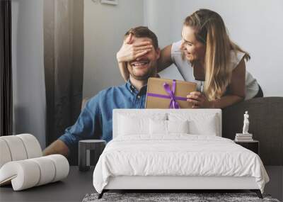 woman giving surprise gift to beloved man at home. closed eyes with hand from behind Wall mural