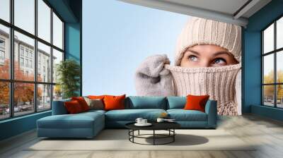 woman in knitted wool clothes hiding her face in sweater and looking up isolated on blue background. winter fashion. warm clothing. banner with copy space Wall mural