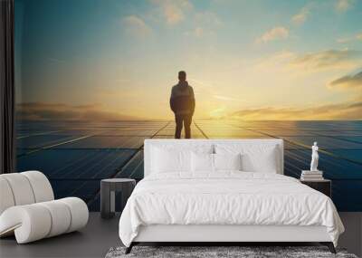 A man stands on a solar panel, looking out at the sunset Wall mural