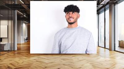 Amazed young arab man with curly hair wearing sport sweatshirt
over white background bitting lip and looking tricky to empty space. Wall mural