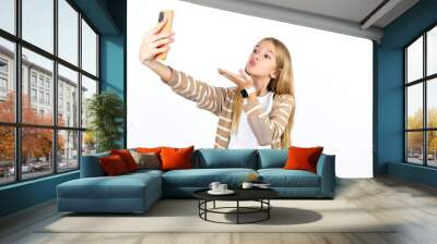 Beautifu blonde kid girl blows air kiss at camera of smartphone and takes selfie, sends mwah via online call. Wall mural