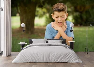 beautiful Caucasian little kid boy wearing blue T-shirt standing outdoors shouting suffocate because painful strangle. Health problem. Asphyxiate and suicide concept. Wall mural