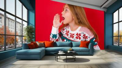 brunette kid girl in knitted sweater christmas over red background look empty space holding hand nea Wall mural