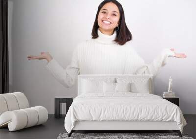 Cheerful cheery optimistic Young brunette woman wearing white knitted sweater against white background holding two palms copy space Wall mural