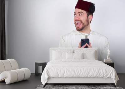 Copyspace photo of young handsome Caucasian man wearing Arab djellaba and Fez hat over white wall stupor with something occurring in social media Wall mural