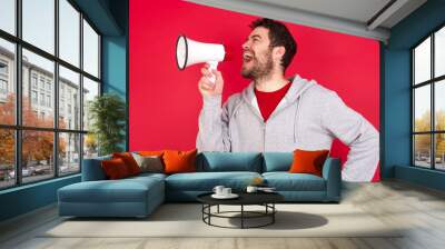 Funny Young caucasian man wearing tracksuit over red background People sincere emotions lifestyle concept. Mock up copy space. Screaming in megaphone. Wall mural