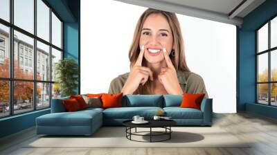 Happy young beautiful woman wearing green overshirt over white background with toothy smile, keeps index fingers near mouth, fingers pointing and forcing cheerful smile Wall mural