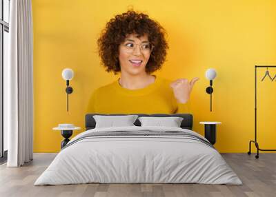 Portrait of Arab businesswoman wearing yellow sweater using and texting with smartphone over isolated background pointing and showing with thumb up to the side with happy face smiling Wall mural