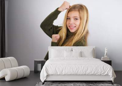 Profile photo of excited Caucasian kid girl wearing green knitted sweater against white wall raising fists celebrating black Friday shopping Wall mural