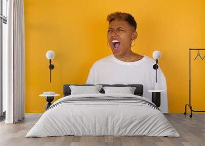 Young Afro American girl with afro short hair wearing white tshirt standing over isolated yellow wall angry and mad screaming frustrated and furious, shouting with anger. Rage and aggressive concept. Wall mural