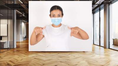 Young arab woman wearing medical mask standing over isolated white background pointing with two fingers at copy space down. Place for advertising Wall mural