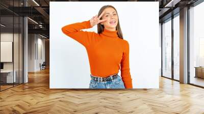 young beautiful girl wearing orange turtleneck Doing peace symbol with fingers over face, smiling cheerful showing victory Wall mural