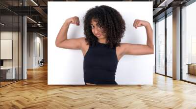 Young beautiful girl with afro hairstyle wearing black tank top over white background showing arms muscles smiling proud. Fitness concept. Wall mural