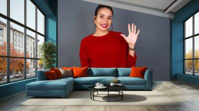 Young beautiful hispanic woman wearing red sweater against gray background showing and pointing up with fingers number five while smiling confident and happy. Wall mural