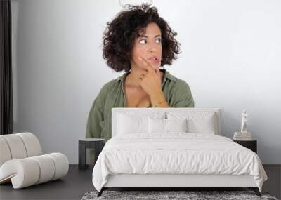 young beautiful woman with curly short hair wearing green overshirt over white wall Thinking worried about a question, concerned and nervous with hand on chin. Wall mural