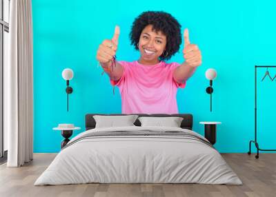 young girl with afro hairstyle wearing pink T-shirt over blue background approving doing positive gesture with hand, thumbs up smiling and happy for success. Winner gesture. Wall mural