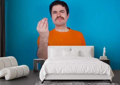 young handsome Caucasian man with moustache wearing orange t-shirt against blue background Doing Italian gesture with hand and fingers confident expression Wall mural