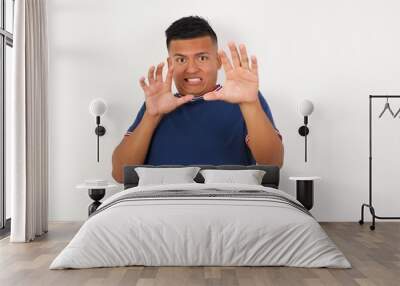 Young handsome hispanic man wearing casual t-shirt standing over white isolated background afraid and terrified with fear expression stop gesture with hands, shouting in shock. Panic concept. Wall mural