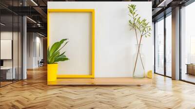 yellow frame with two tropical plant green fresh dracaena houseplant in a flowerpot and dry Eucalyptus branch in glass vase against white wall on a wooden table Wall mural