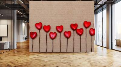 Small red hearts lie in a row on a craft background. Greeting card for Valentine's day in red colors. Background for text. Wall mural