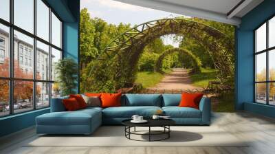 Two arches with plants growing on them in a park with a path going under them Wall mural