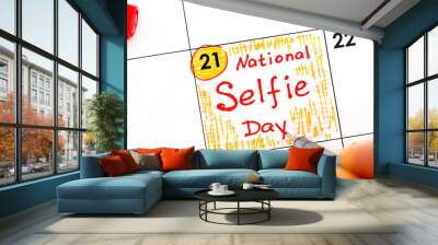 Woman fingers with pen writing reminder National Selfie Day in calendar. Wall mural