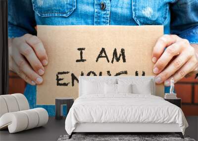 Woman hands holding a piece of a cardboard with words I am Enough Wall mural